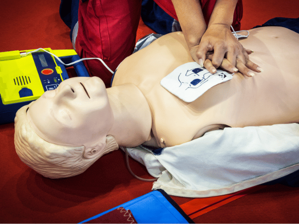 CPR training mannequin receiving chest compressions with AED pads during BLS CPR practice